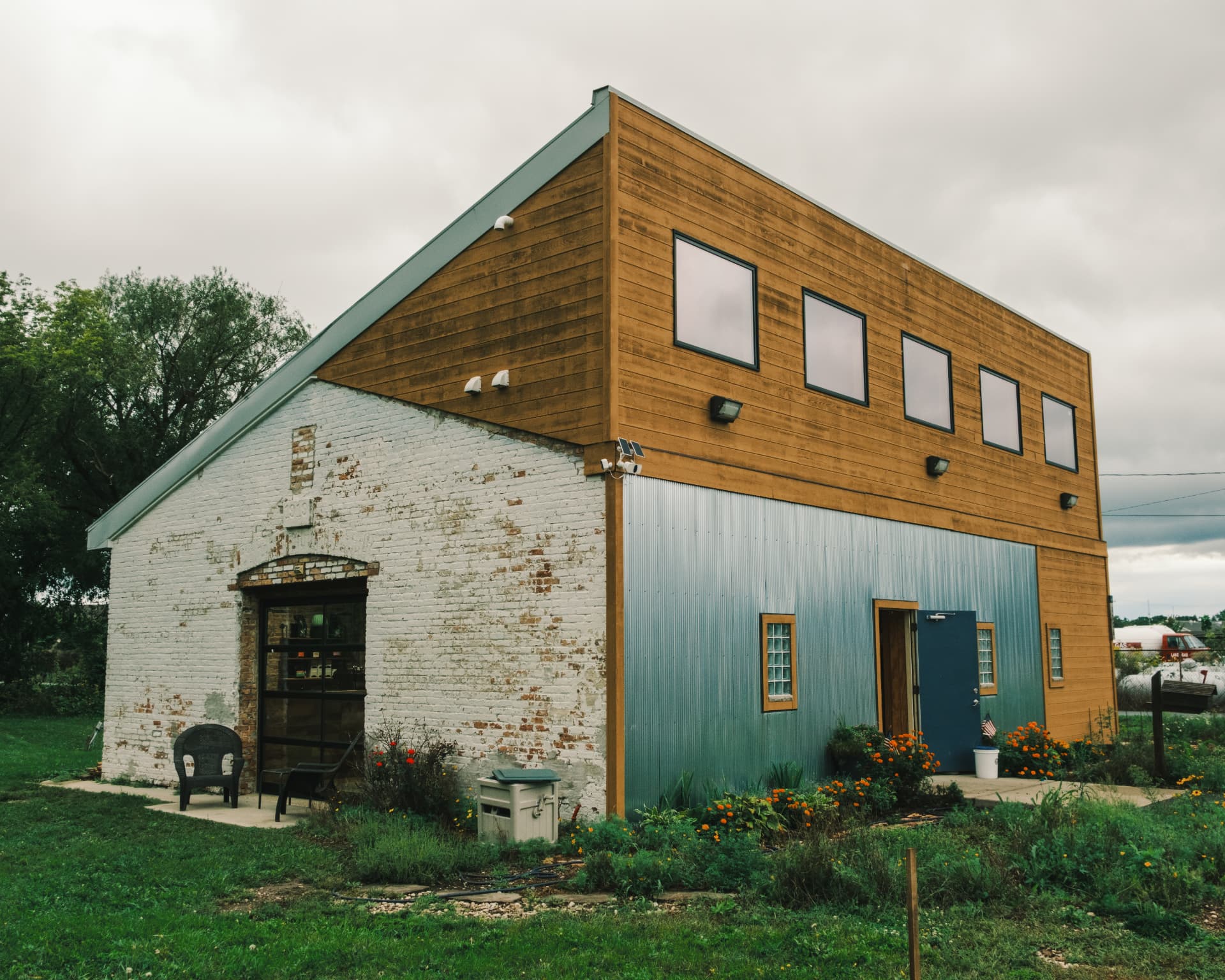 The DSCO Coffee shop, a white brick barn with timber siding and a glass garage door, seen from the lawn