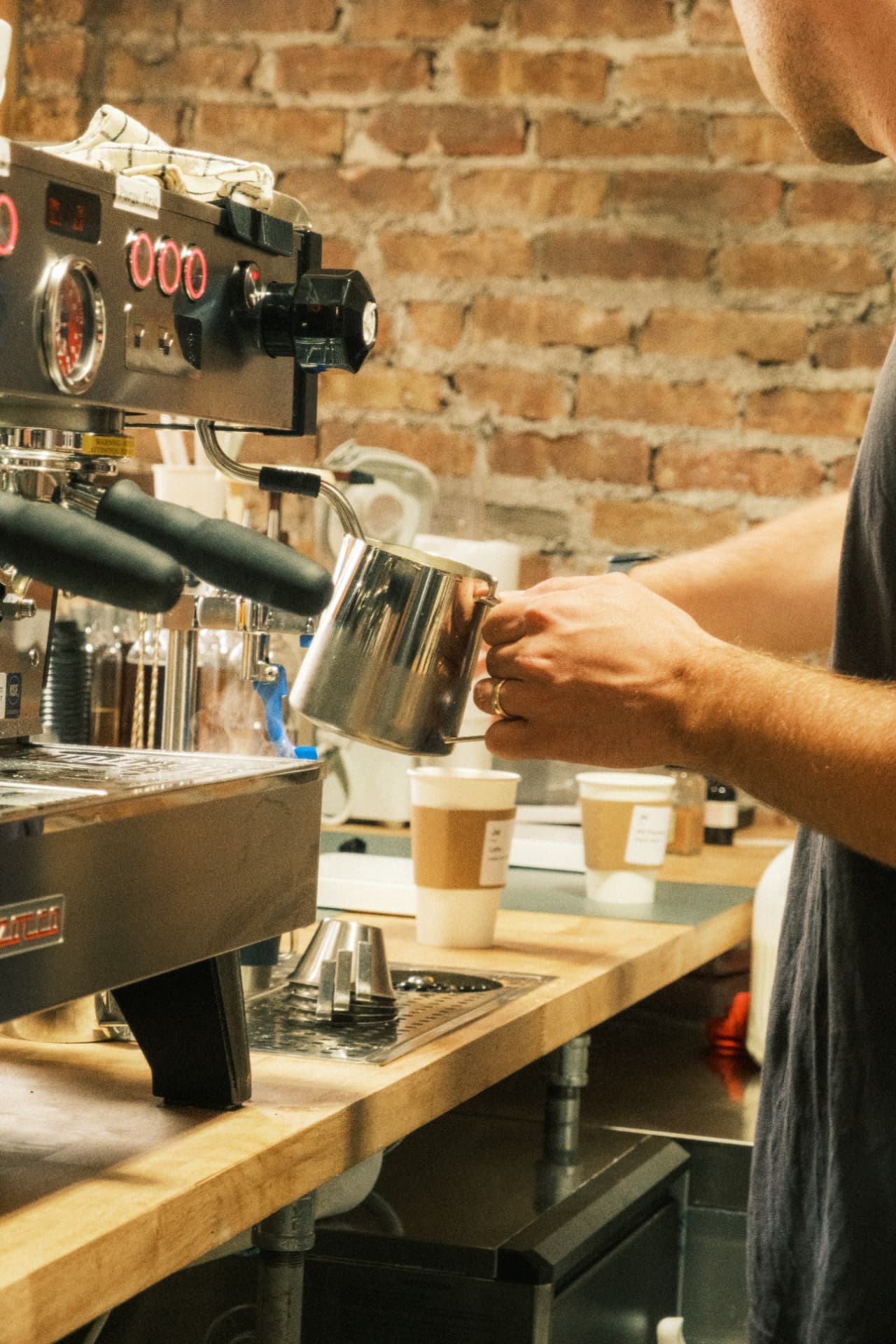 A barista steaming milk beside the espresso machine